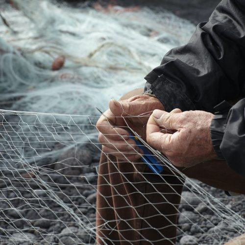 Fisherman repairing net on pebble beach